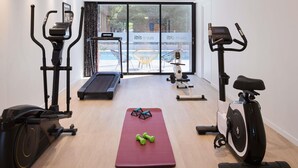 Ein Fitnessraum mit Laufbändern, Crosstrainern, einem Ergometer und einer Yogamatte.