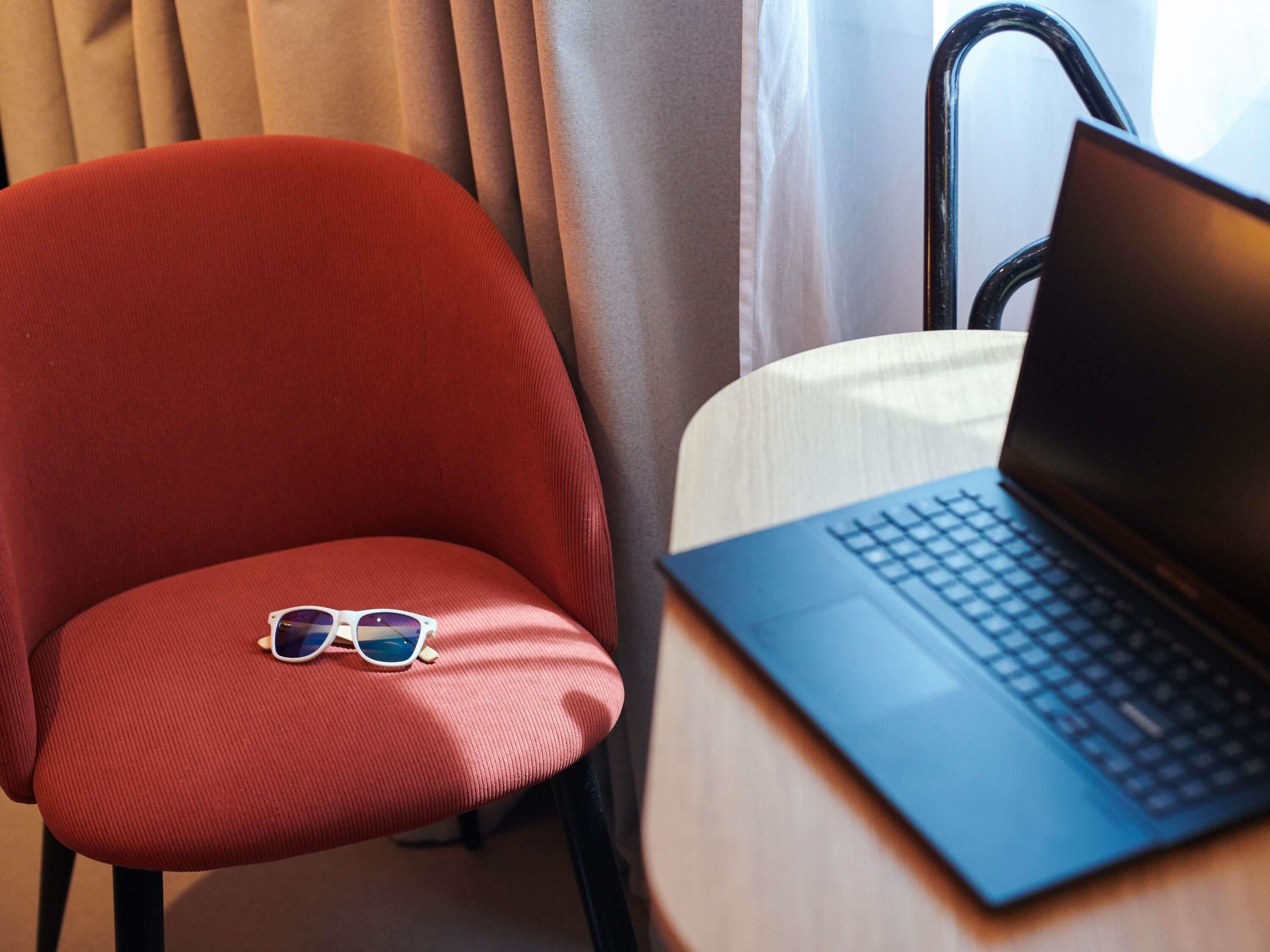 A red chair with sunglasses on it and a laptop on a table.