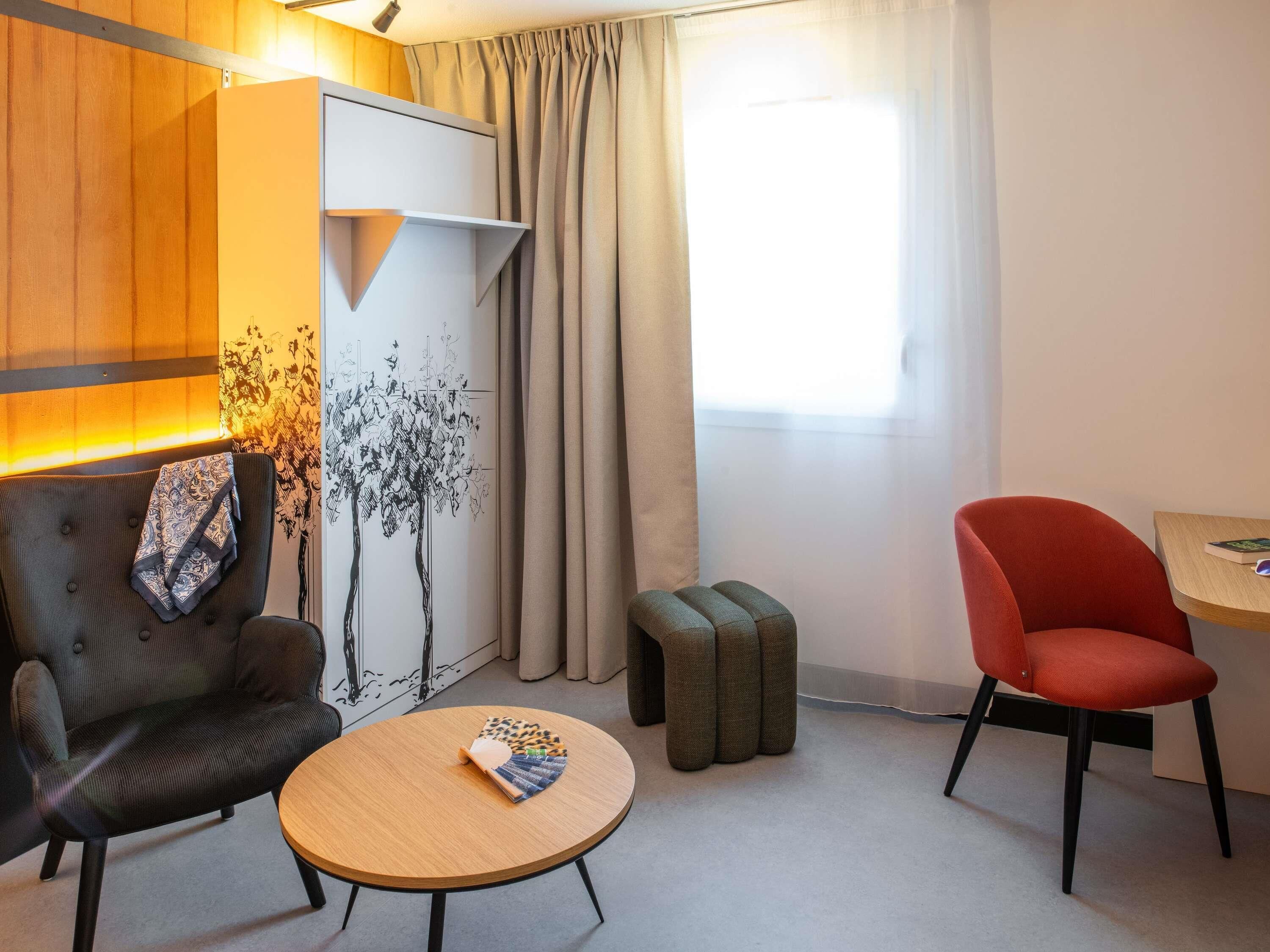 Una habitación moderna con sofá, una silla roja, una mesita y una ventana con cortinas.