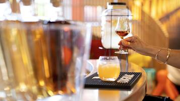 Zona de bar con una persona sosteniendo una copa de vino, una grifería y un vaso de jugo de naranja sobre un posavasos.