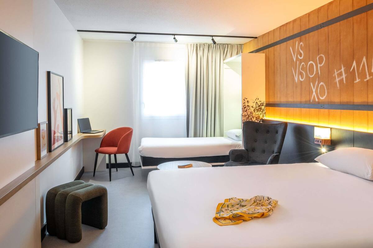 Ett hotellrum med en säng, ett skrivbord, en stol och en liten pall.