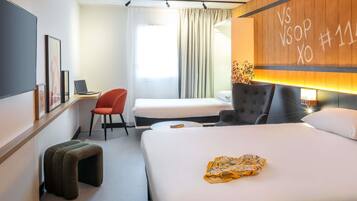 A hotel room with a bed, a desk, a chair, and a small stool.