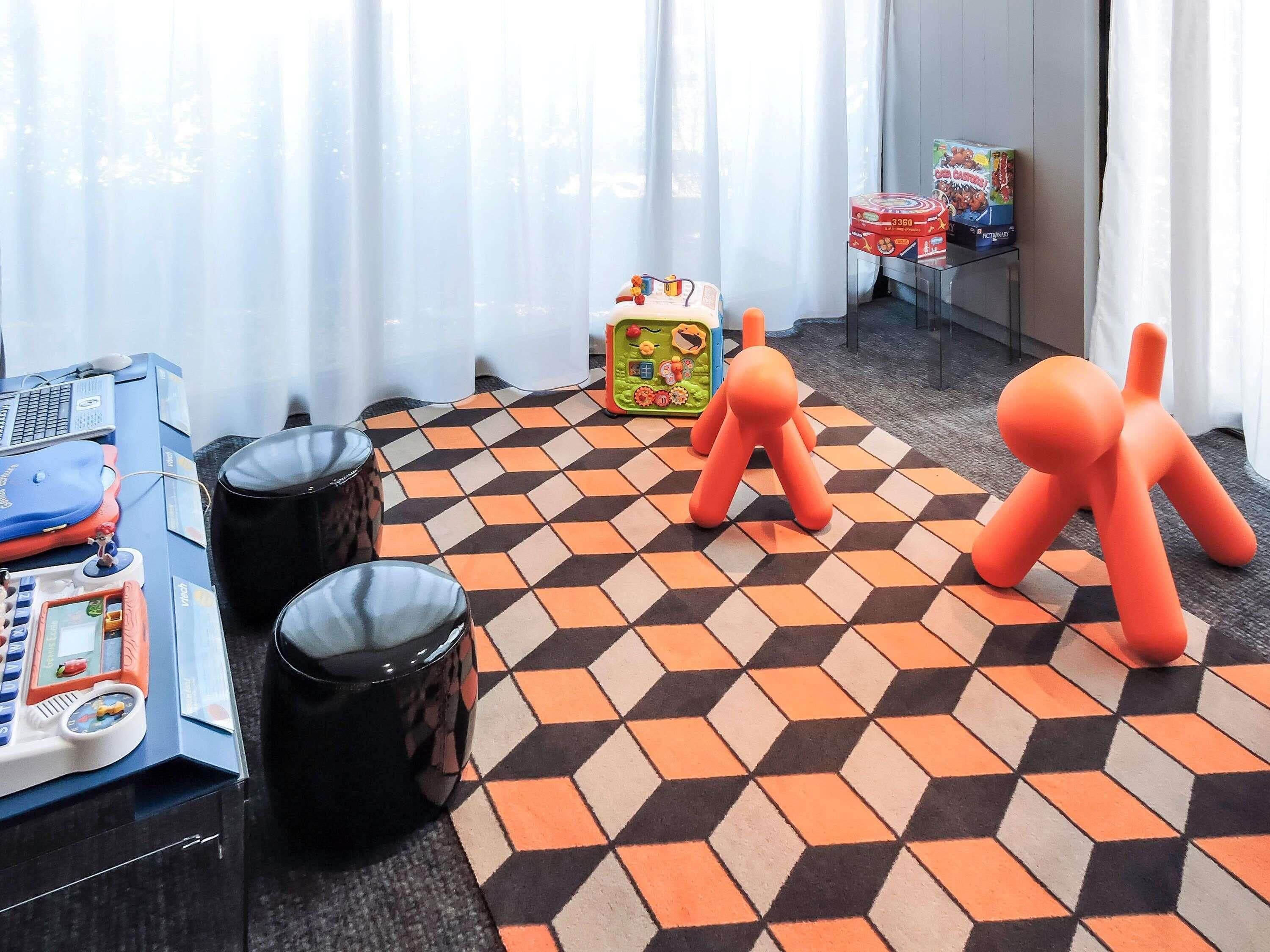 A room with a checkered floor, a desk with a computer, two trash bins, and a window with curtains.