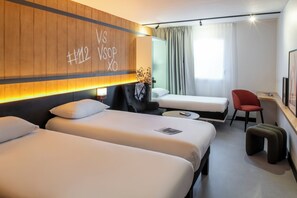 A hotel room with two beds, a desk, a chair, and a window with curtains.