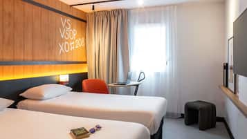 Une chambre d’hôtel avec deux lits, un bureau avec un ordinateur portable, une chaise, une télévision et une fenêtre avec des rideaux.