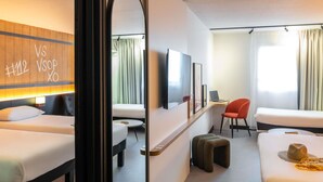 Ein Hotelzimmer mit zwei Betten, einem Schreibtisch, einem Stuhl, einem Fernseher und einem Spiegel.
