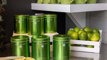 A display of green tea products, including tins and cups, with a box of limes on a metallic surface.