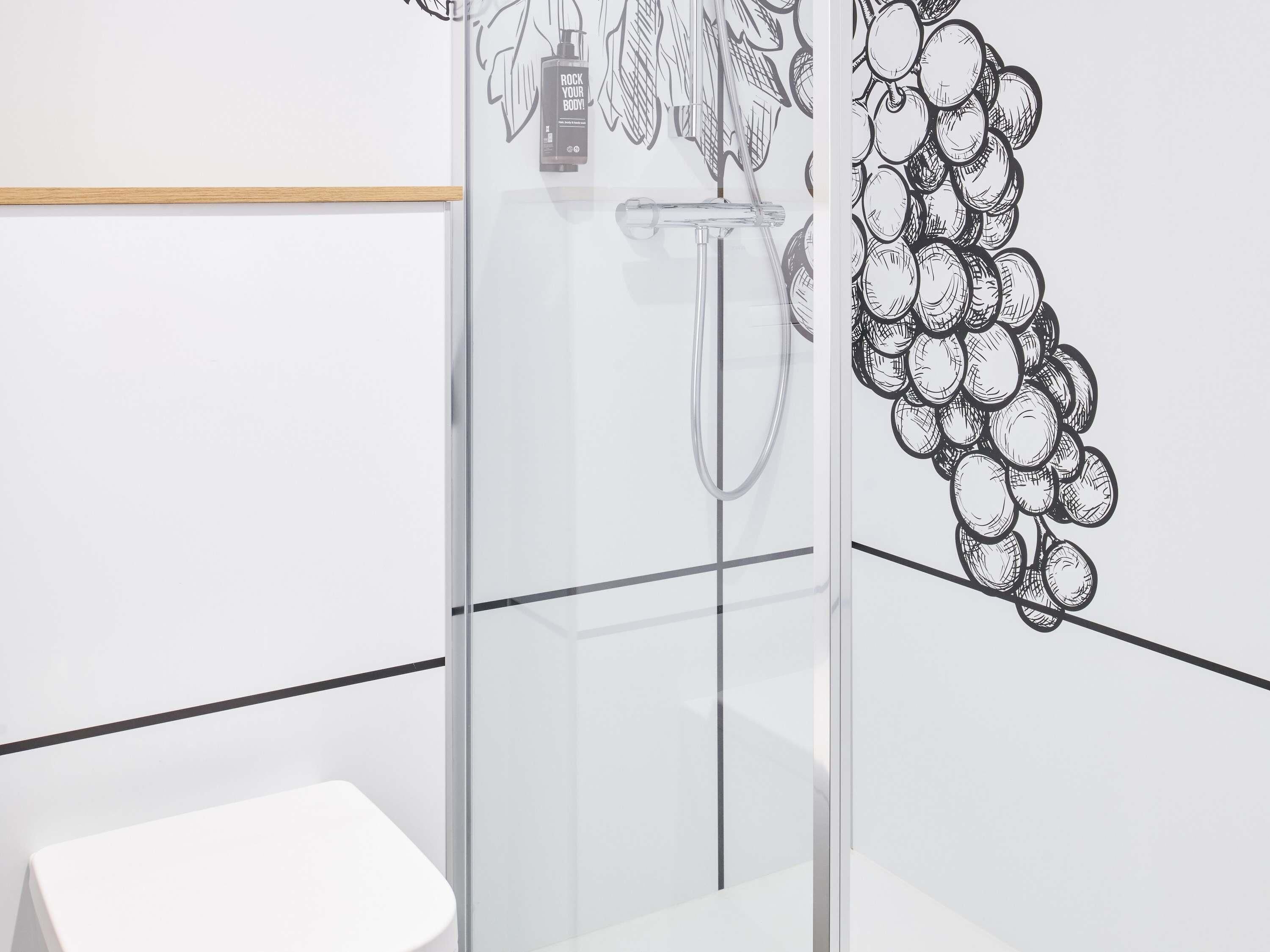 A modern bathroom with a glass shower enclosure, a white sink, and a wall with a grape illustration.