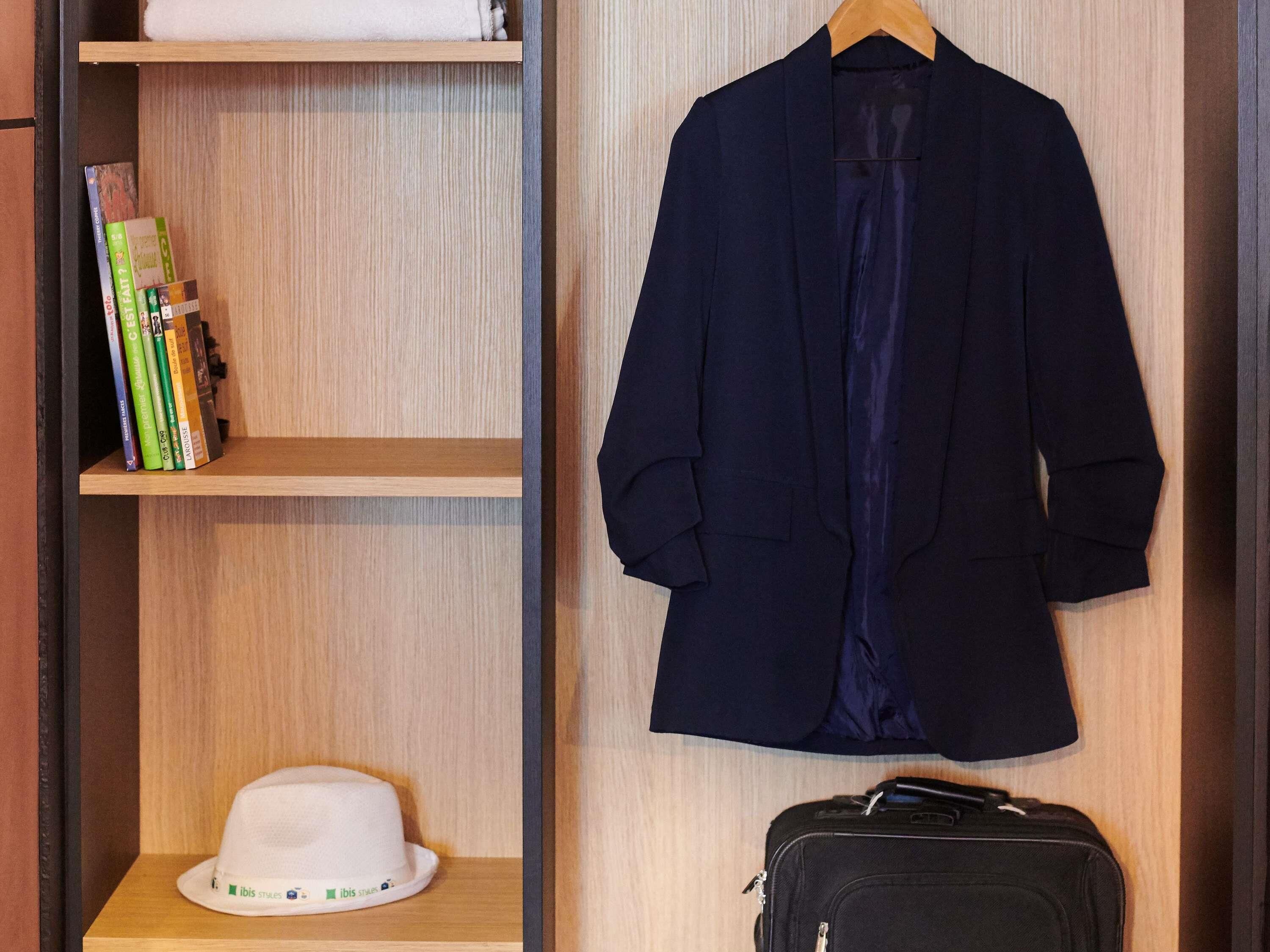A wooden wardrobe with a hanging coat, a hat, and a suitcase.