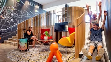 Un interior moderno con un mural de mapas, una silla roja, una silla amarilla y una persona sentada en un tobogán.