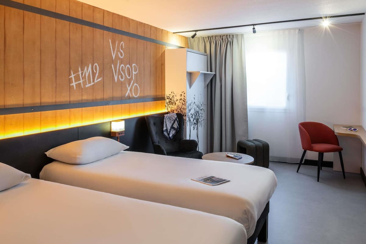 Ett hotellrum med två sängar, ett skrivbord, en stol och en vägg med ett dekorativt element.