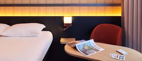A hotel room with a bed, a table with a magazine and playing cards, and a wall with 'VS VSOP XO 304+' written on it.