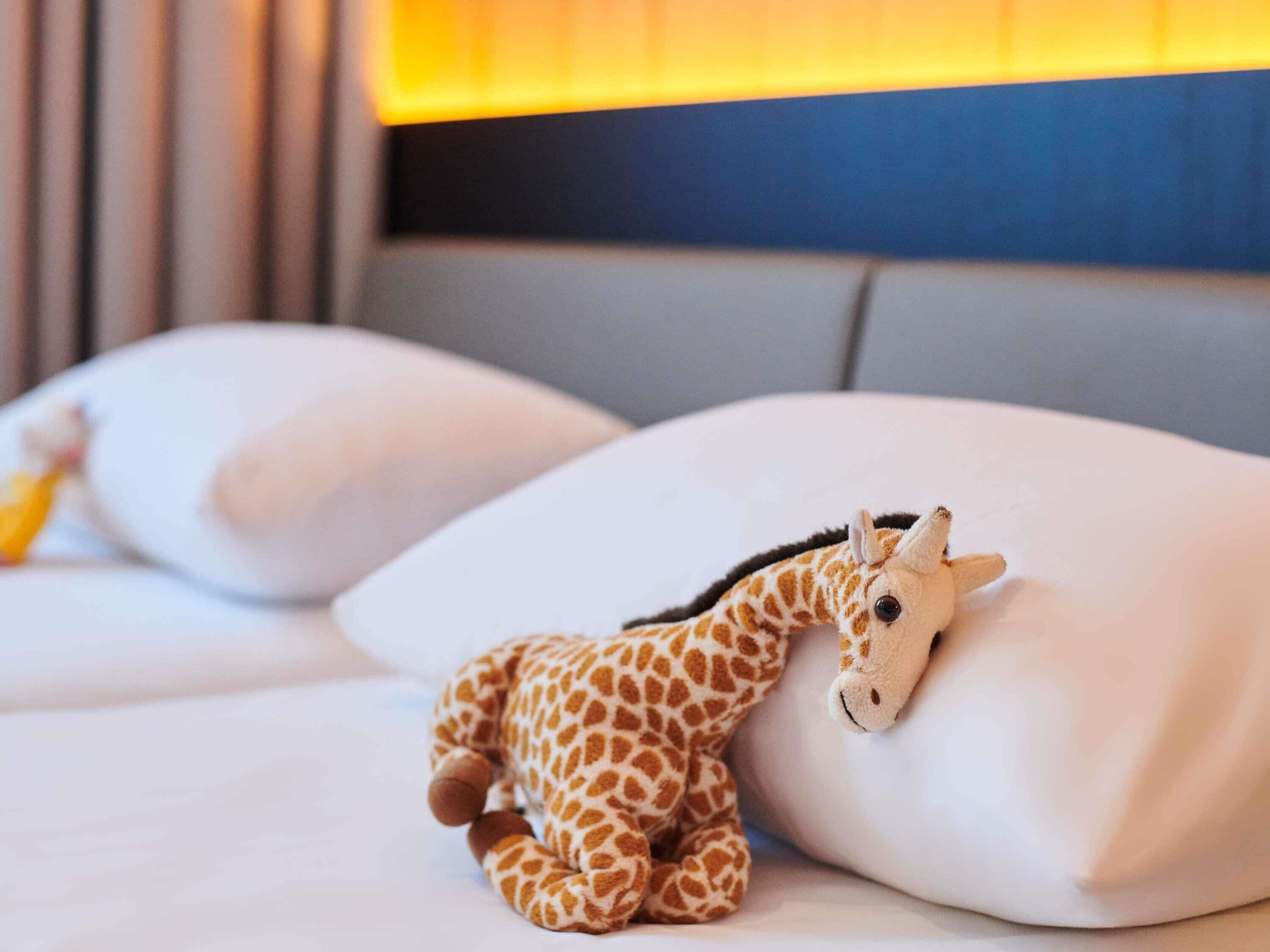 Un lit avec des oreillers blancs et une petite peluche en forme de girafe posée sur l’un des oreillers.