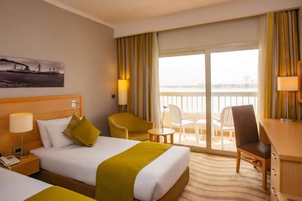 Une chambre d’hôtel avec deux lits, un bureau, une chaise, une petite table et un balcon avec vue.
