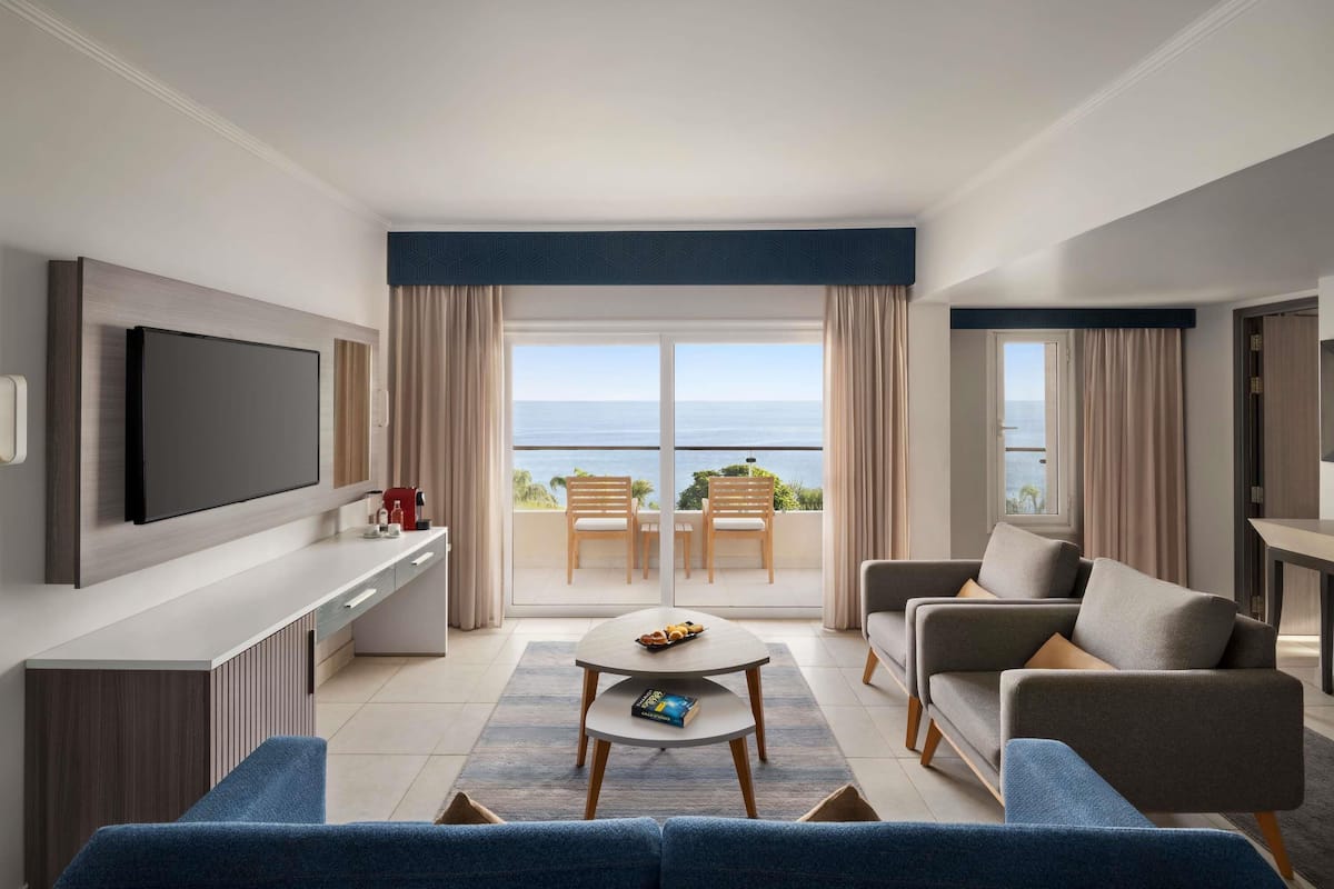 Un salon moderne doté d’un téléviseur à écran plat, d’un canapé, d’une table basse et d’un balcon offrant une vue sur la mer.