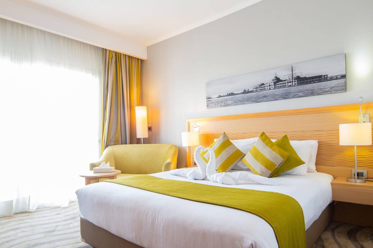 Une chambre d’hôtel avec un grand lit, une chaise, un bureau et un tableau au mur.