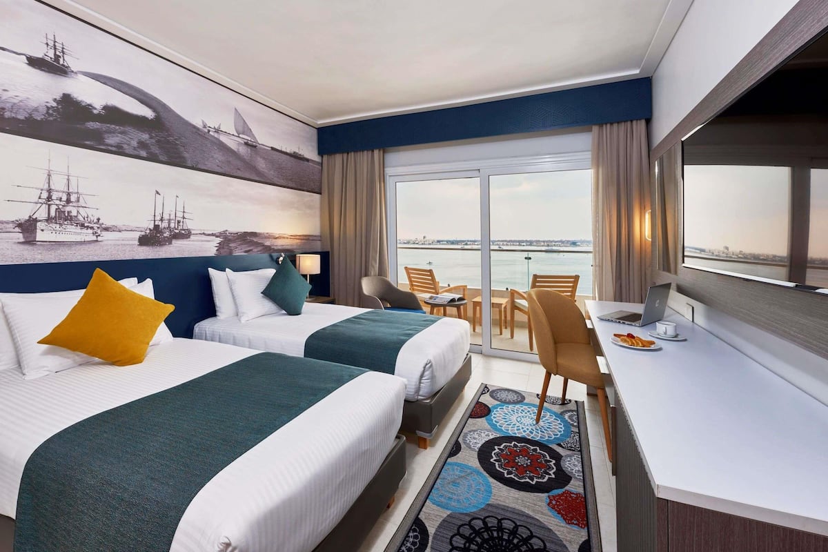 Une chambre d’hôtel avec deux lits, un bureau avec un ordinateur portable, une chaise et une vue sur la mer.