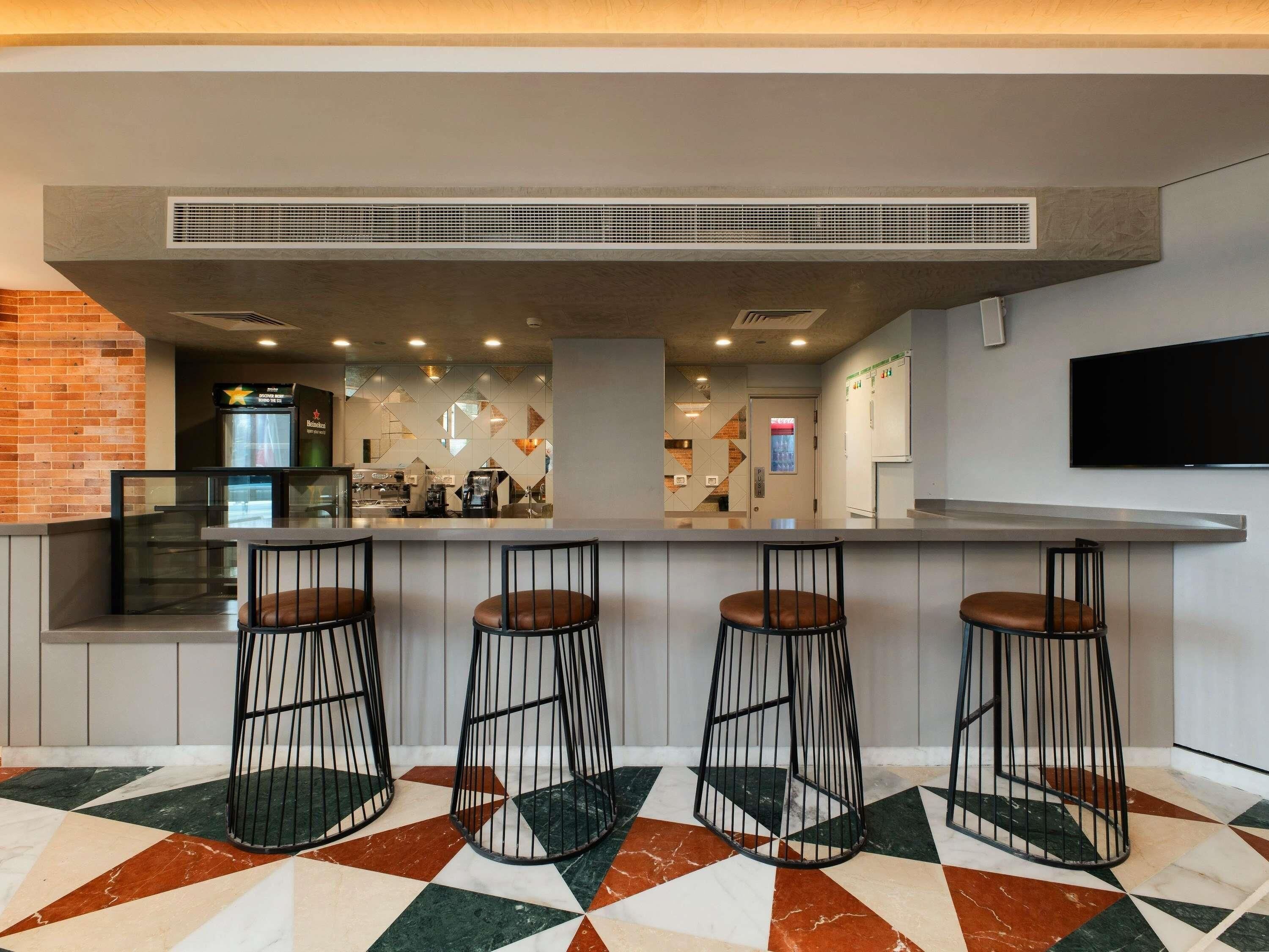 A bar area with a counter, three stools, a television mounted on the wall, and a patterned floor.