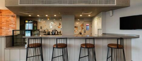 A bar area with a counter, three stools, a television mounted on the wall, and a patterned floor.