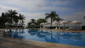 A swimming pool with lounge chairs and umbrellas, surrounded by palm trees and a view of the sea. - Mercure Ismailia Forsan Island Hotel (Ismailia)
