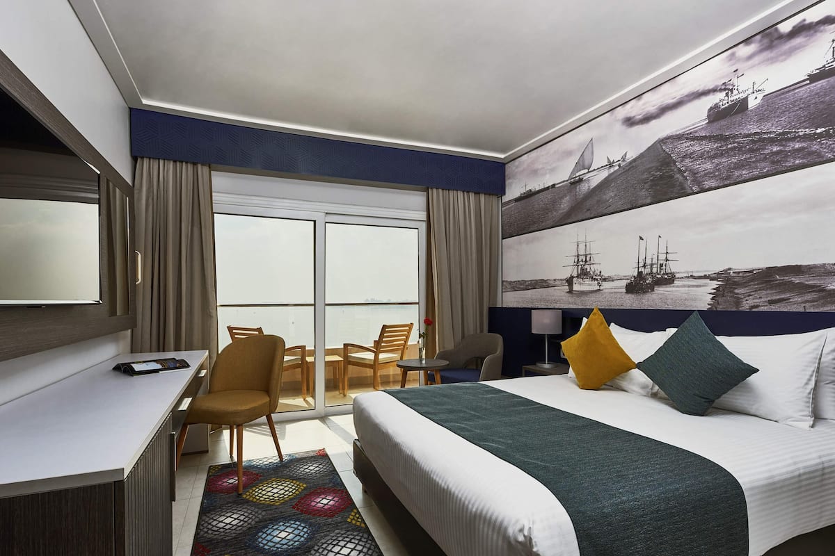 Une chambre d’hôtel avec un lit, un bureau, une chaise, une télévision et une grande fenêtre.