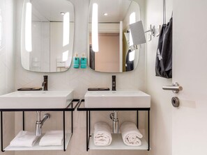 Baño con dos lavamanos, espejos, toalleros y una puerta con una toalla colgada.