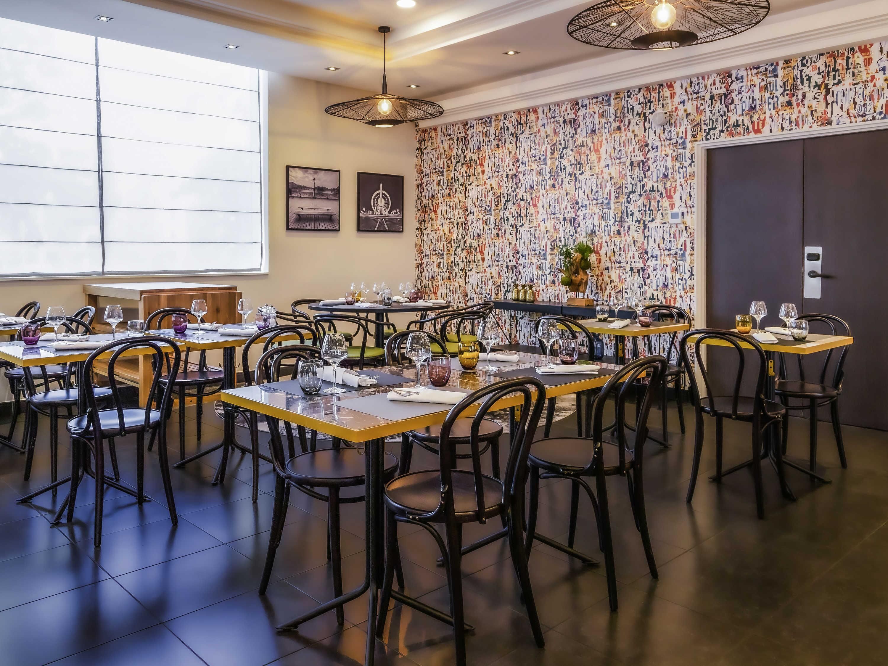 A restaurant with multiple tables and chairs, a patterned wall, and a large window.