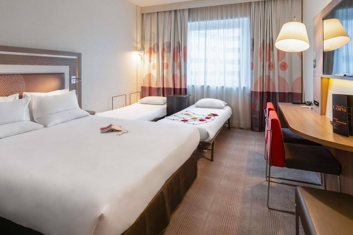 A hotel room with two beds, a desk, and a chair.