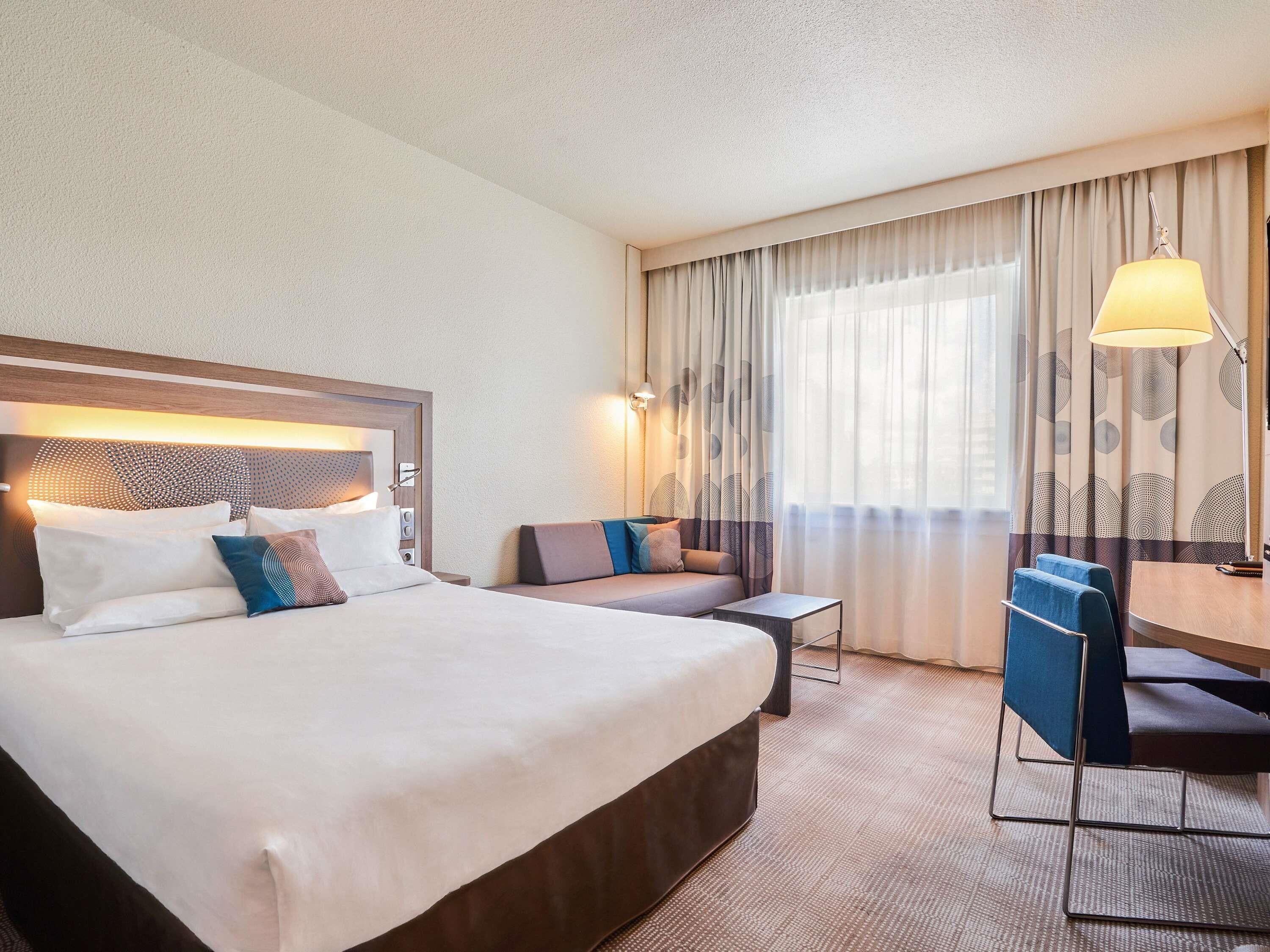 A hotel room with a large bed, a desk, a chair, and a sofa.