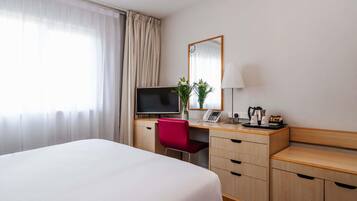 A hotel room with a bed, a desk with a TV, a chair, a lamp, a phone, and a coffee maker.