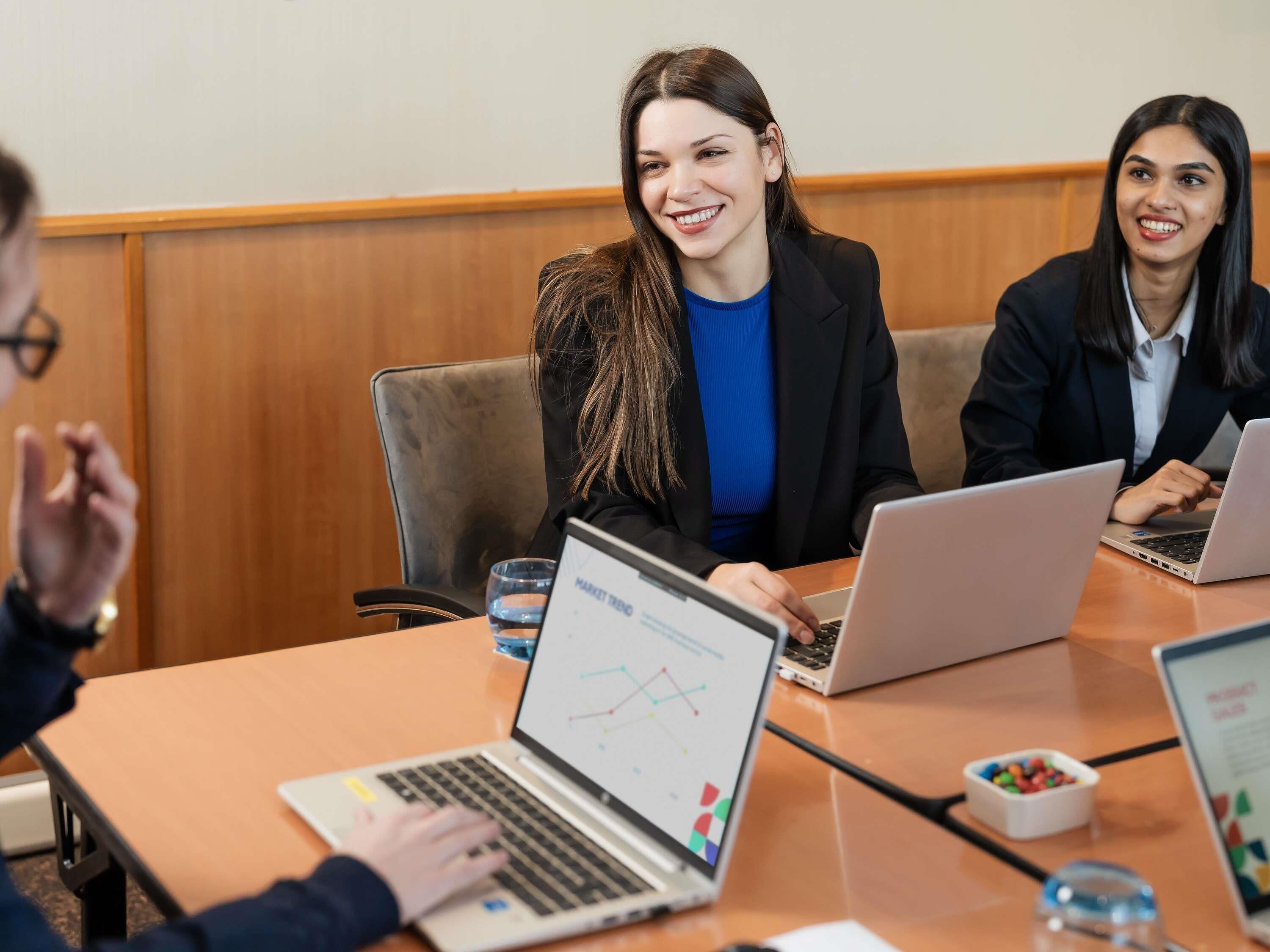 A conference room with a wooden paneled wall, a table with laptops, and a glass of water.