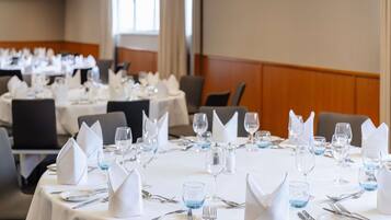 Un comedor de hotel con mesas redondas dispuestas para el servicio, cada una con mantel blanco, cubiertos y vasos de agua azules.