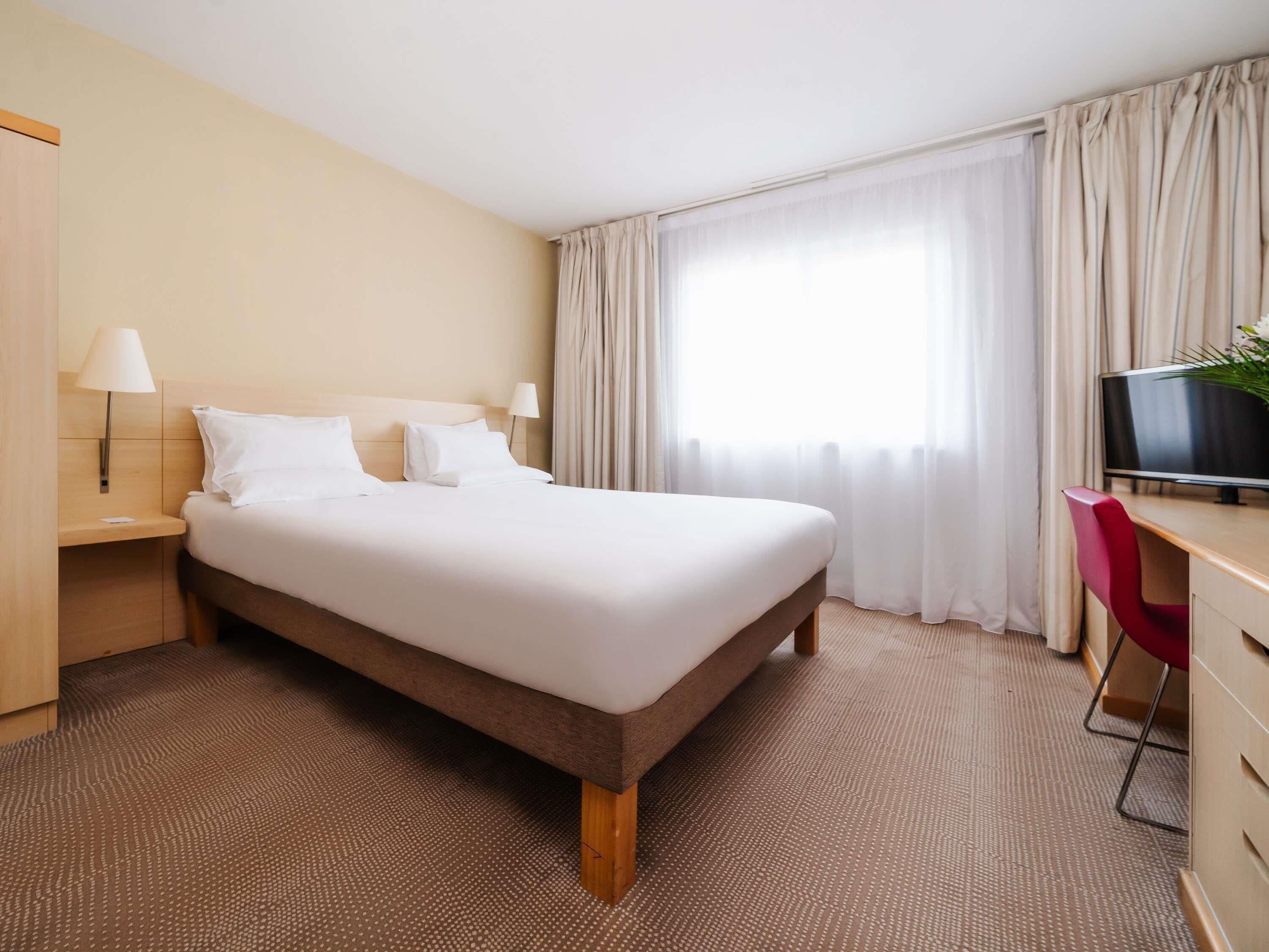 Habitació d'hotel amb un llit gran, un escriptori amb una televisió i una cadira.