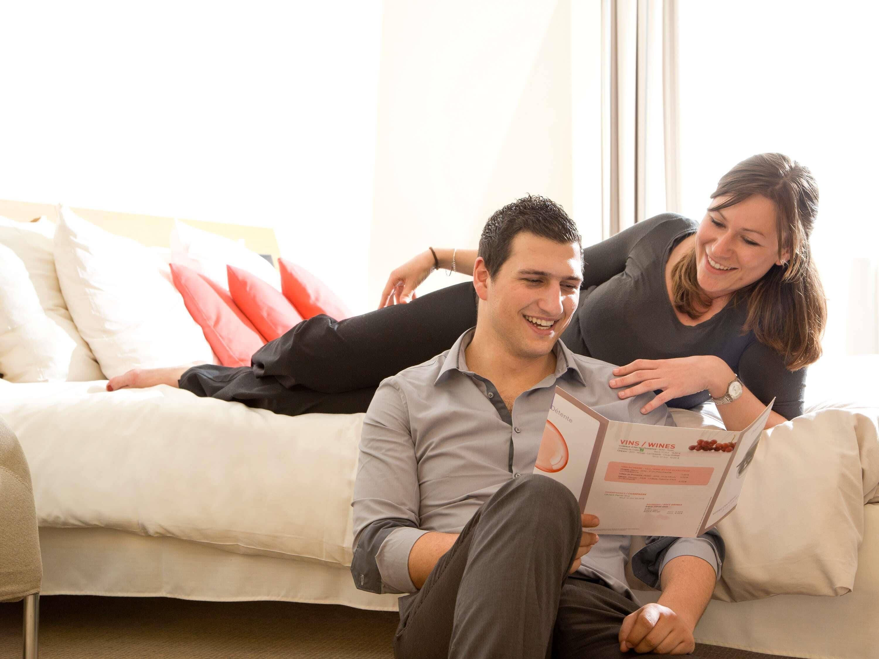 A person sitting on a sofa reading a magazine, with another person leaning over them.