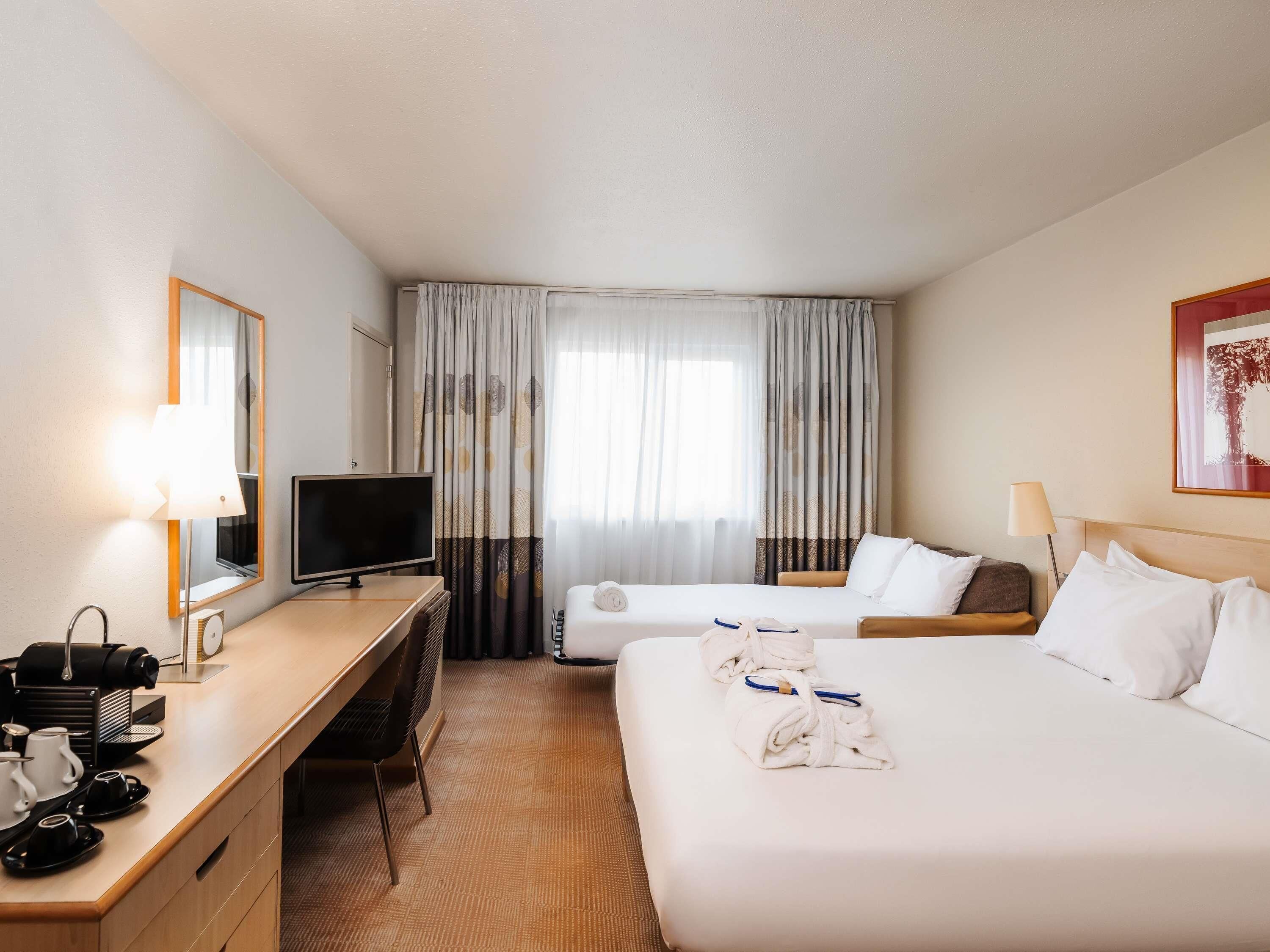 Habitación de hotel con cama, mesita de noche, televisor y escritorio con silla.