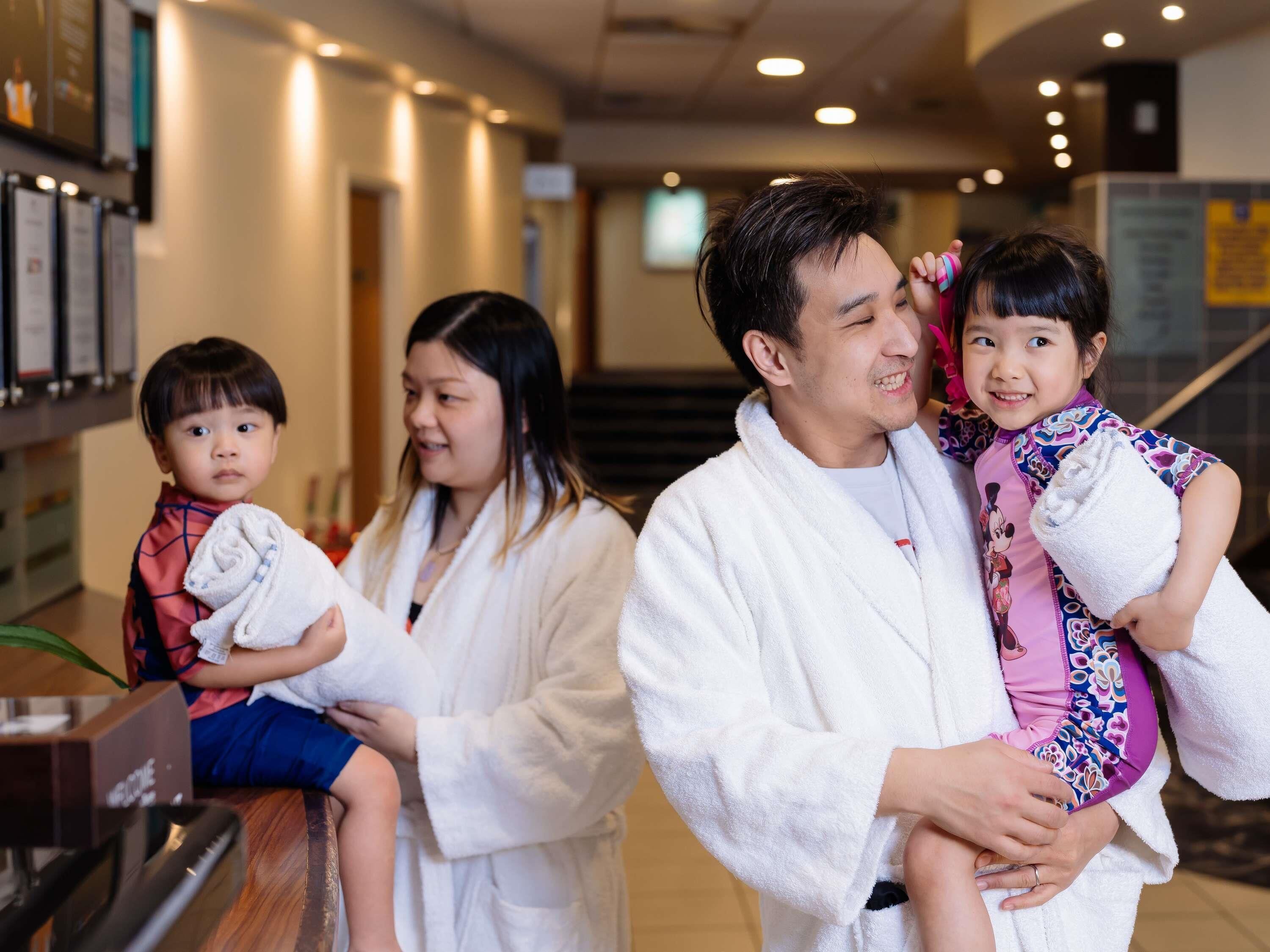 A family in a hotel lobby with a reception desk, a staircase, and a television screen.