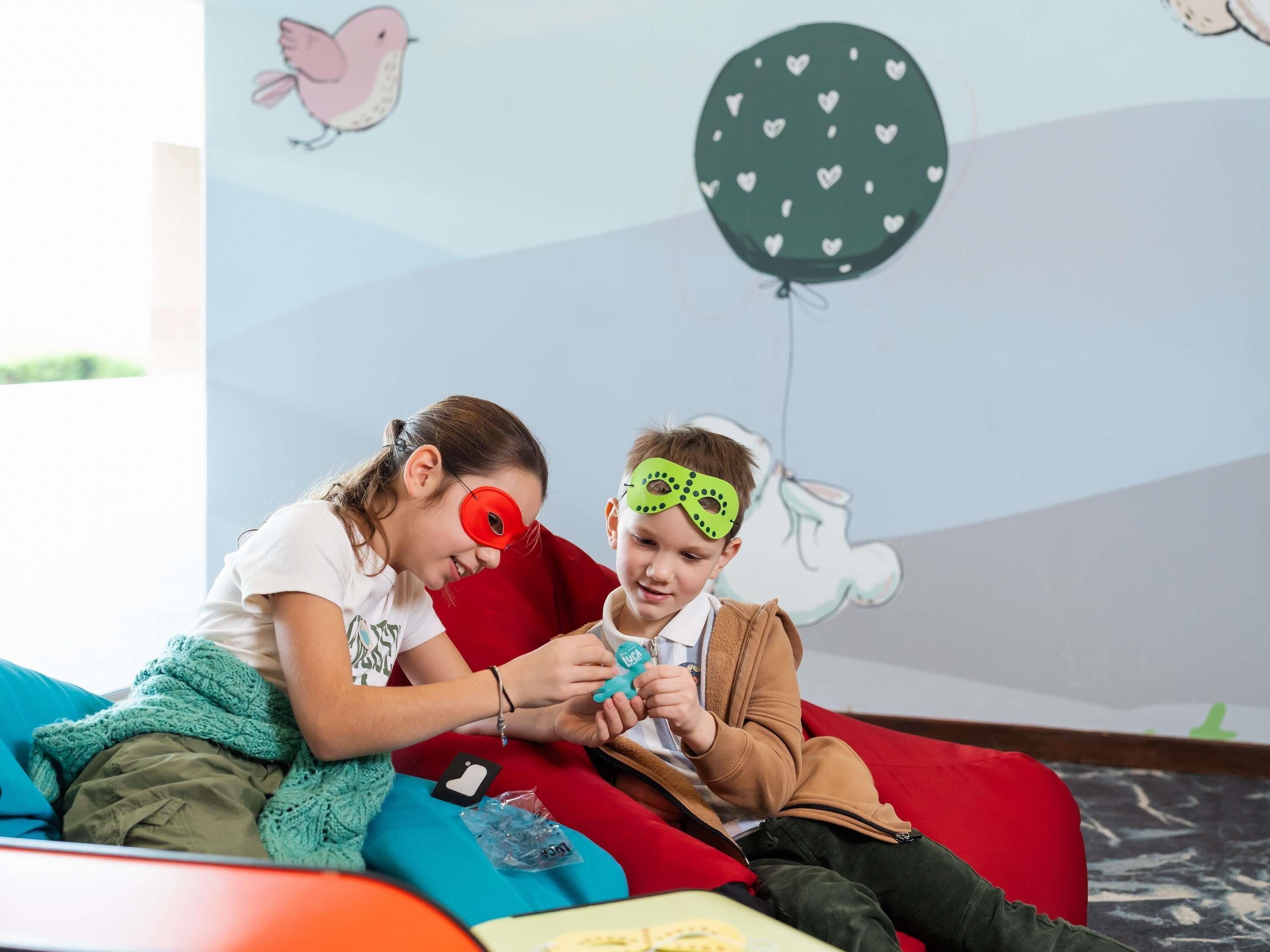 A child and an adult sitting on a colorful couch with a wall mural in the background.