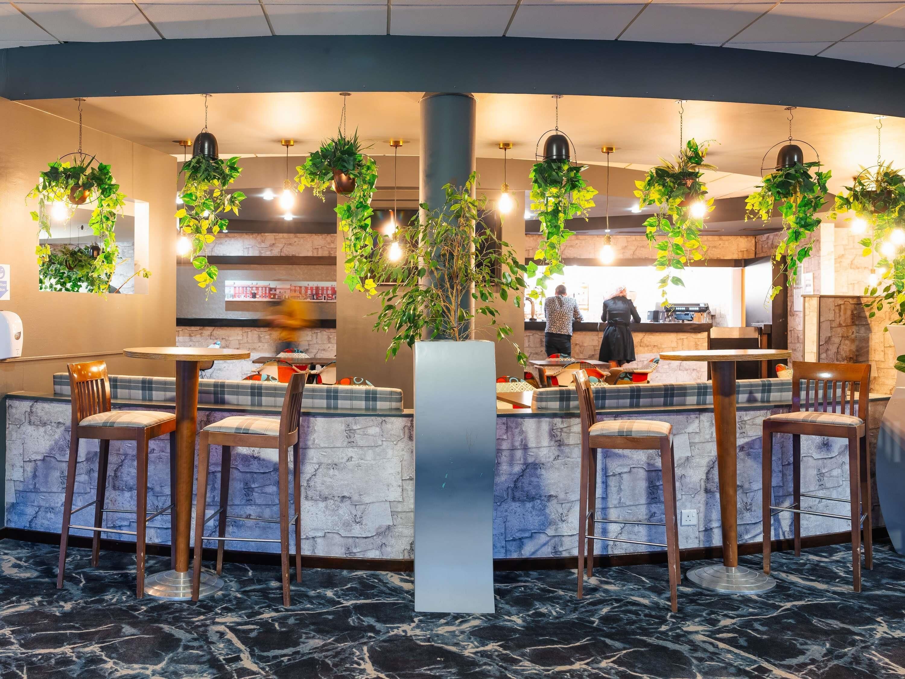 Ein Restaurant mit Marmorboden, Barhocker, hängenden Pflanzen und einer Theke, an der eine Person bedient.