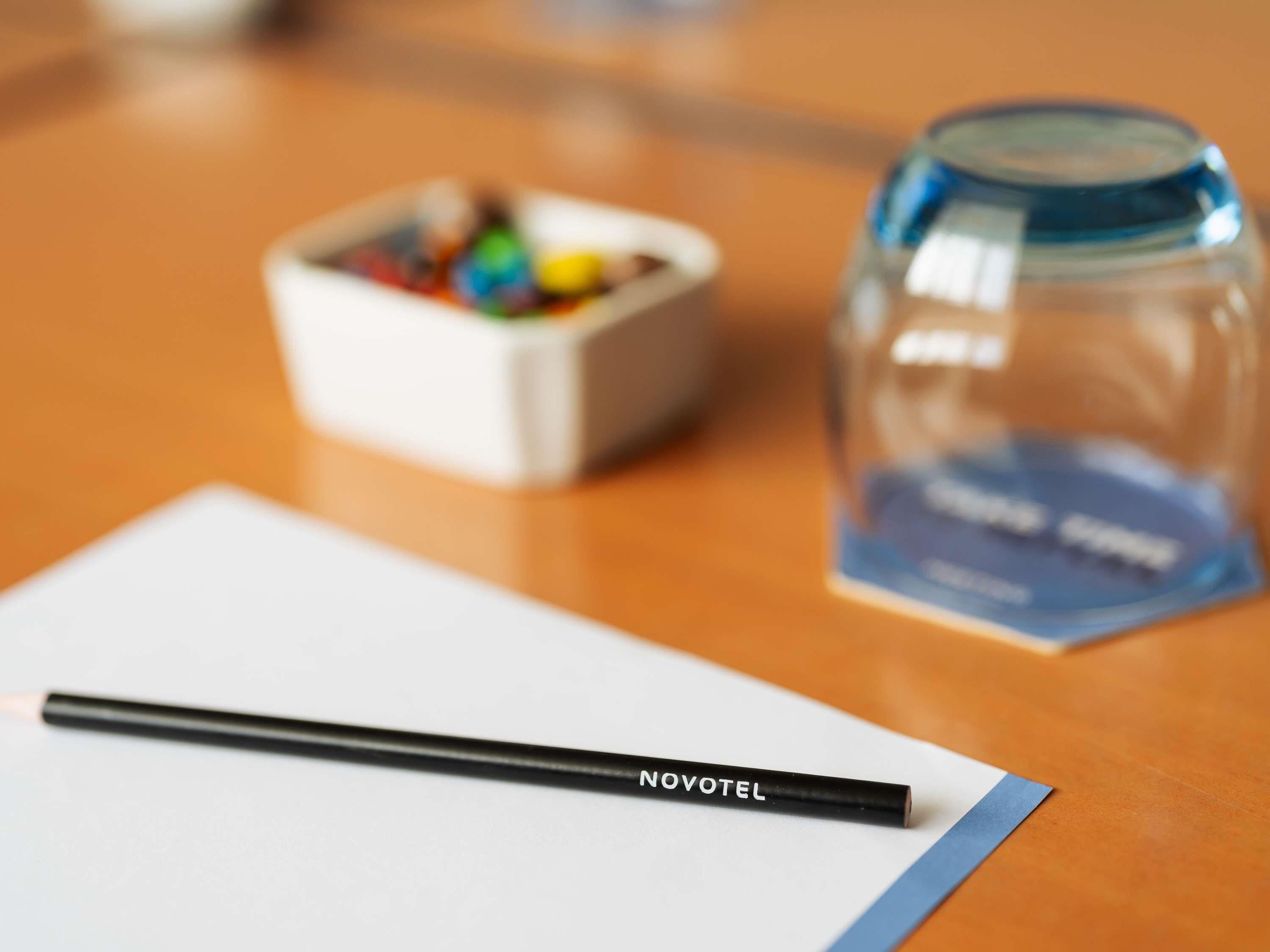 Un escritorio con un lápiz negro, un recipiente pequeño con objetos de colores y un frasco de vidrio transparente con etiqueta azul.