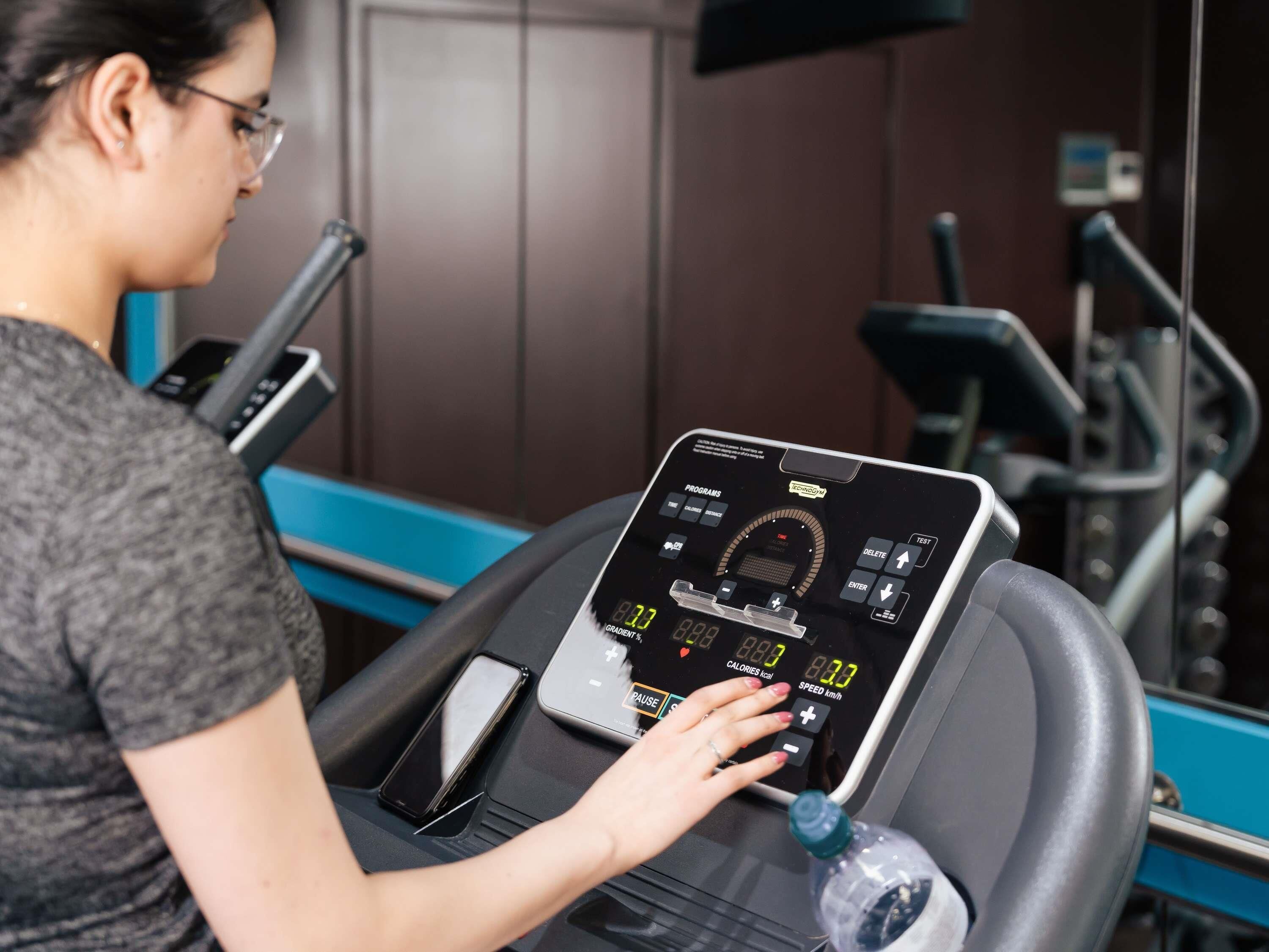 A woman using a stationary bike with a digital display, a water bottle, and a smartphone on the bike's handlebar.