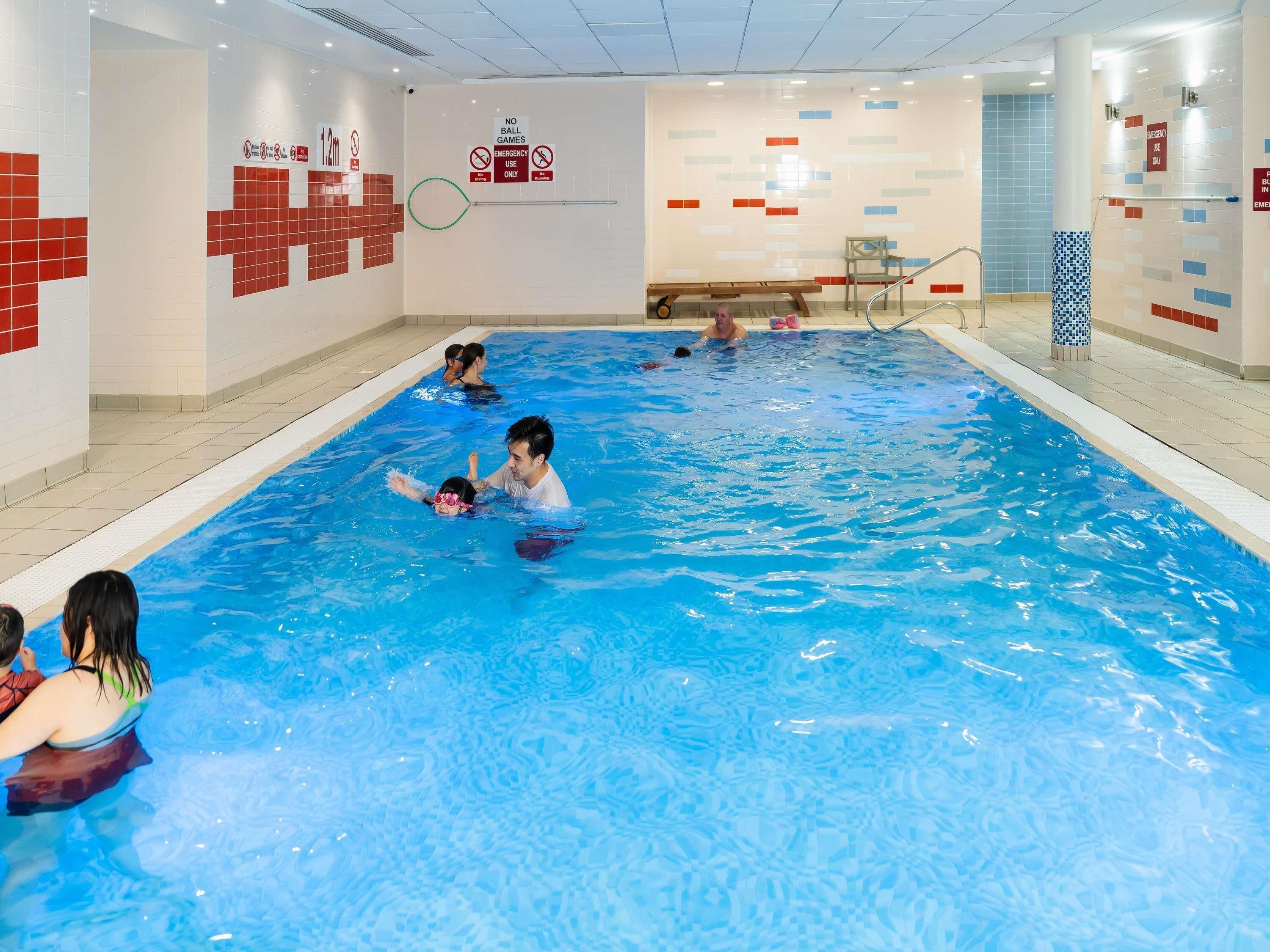 Una piscina interior con paredes de azulejos, un banco y una barandilla.