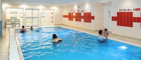 An indoor swimming pool with clear water, tiled walls, and a clock on the wall.