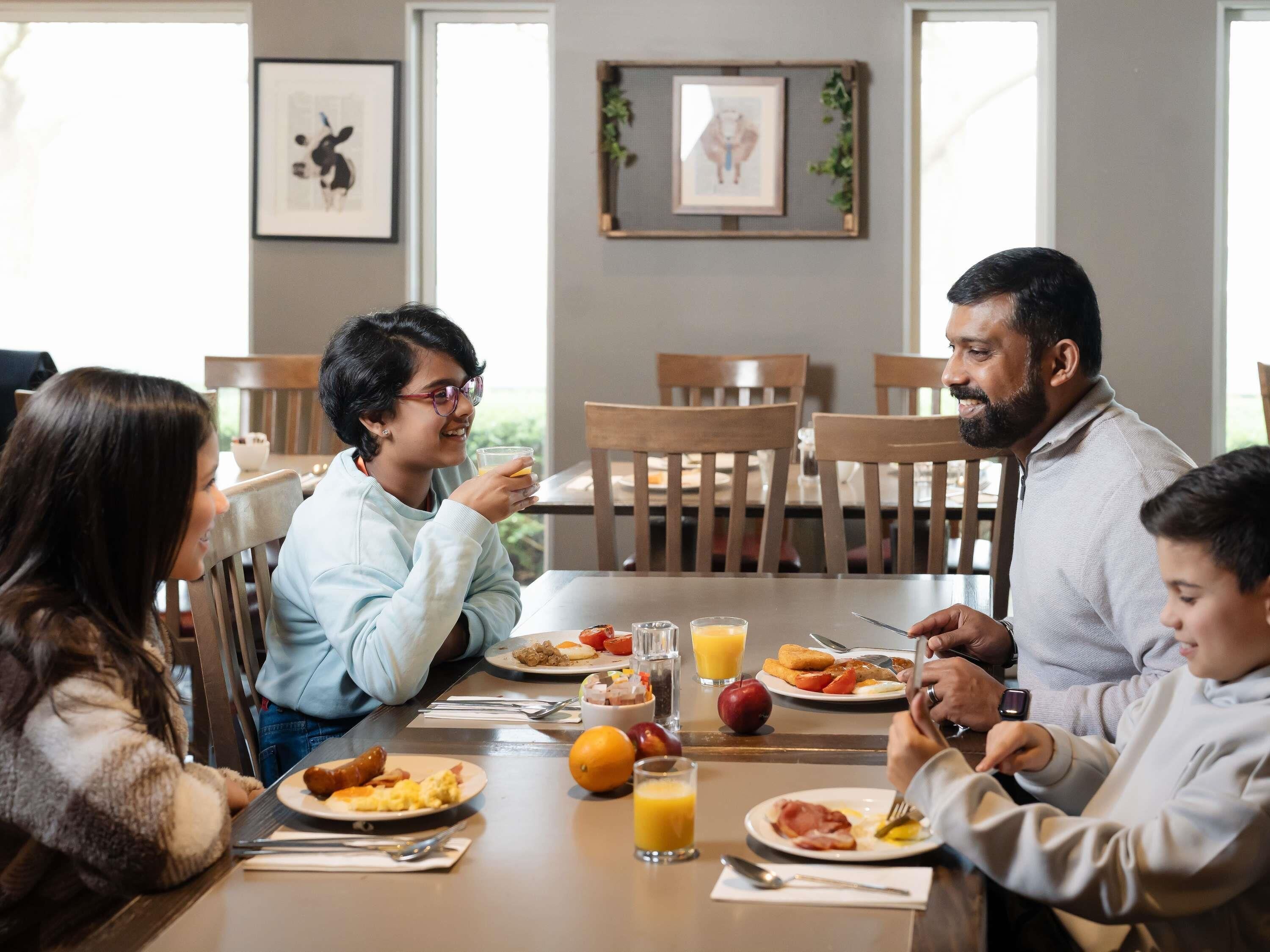 A dining area with wooden chairs, a table with breakfast plates, glasses of orange juice, and framed pictures on the wall.