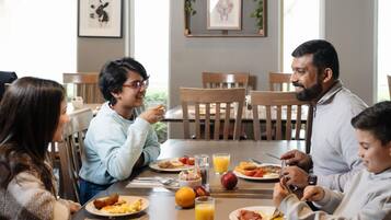 A dining area with wooden chairs, a table with breakfast plates, glasses of orange juice, and framed pictures on the wall.