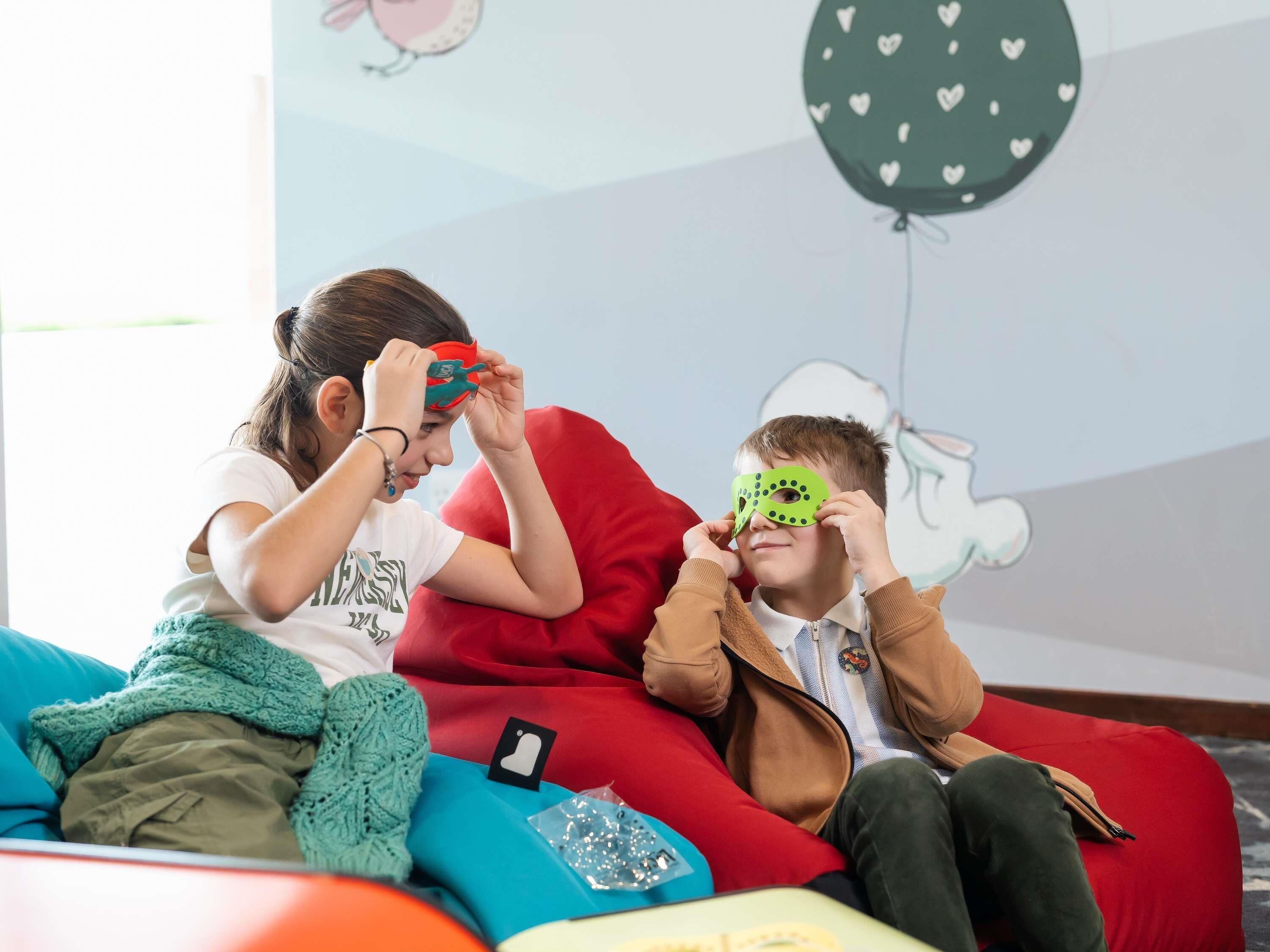 Two individuals seated on bean bags in a room with a wall decorated with heart patterns and a cartoon character.