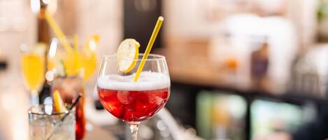 Un bancone bar con un bicchiere di cocktail rosso con ghiaccio, una fetta di limone e una cannuccia.