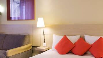 A hotel room with a bed, a nightstand, a lamp, a couch, and a window with curtains.