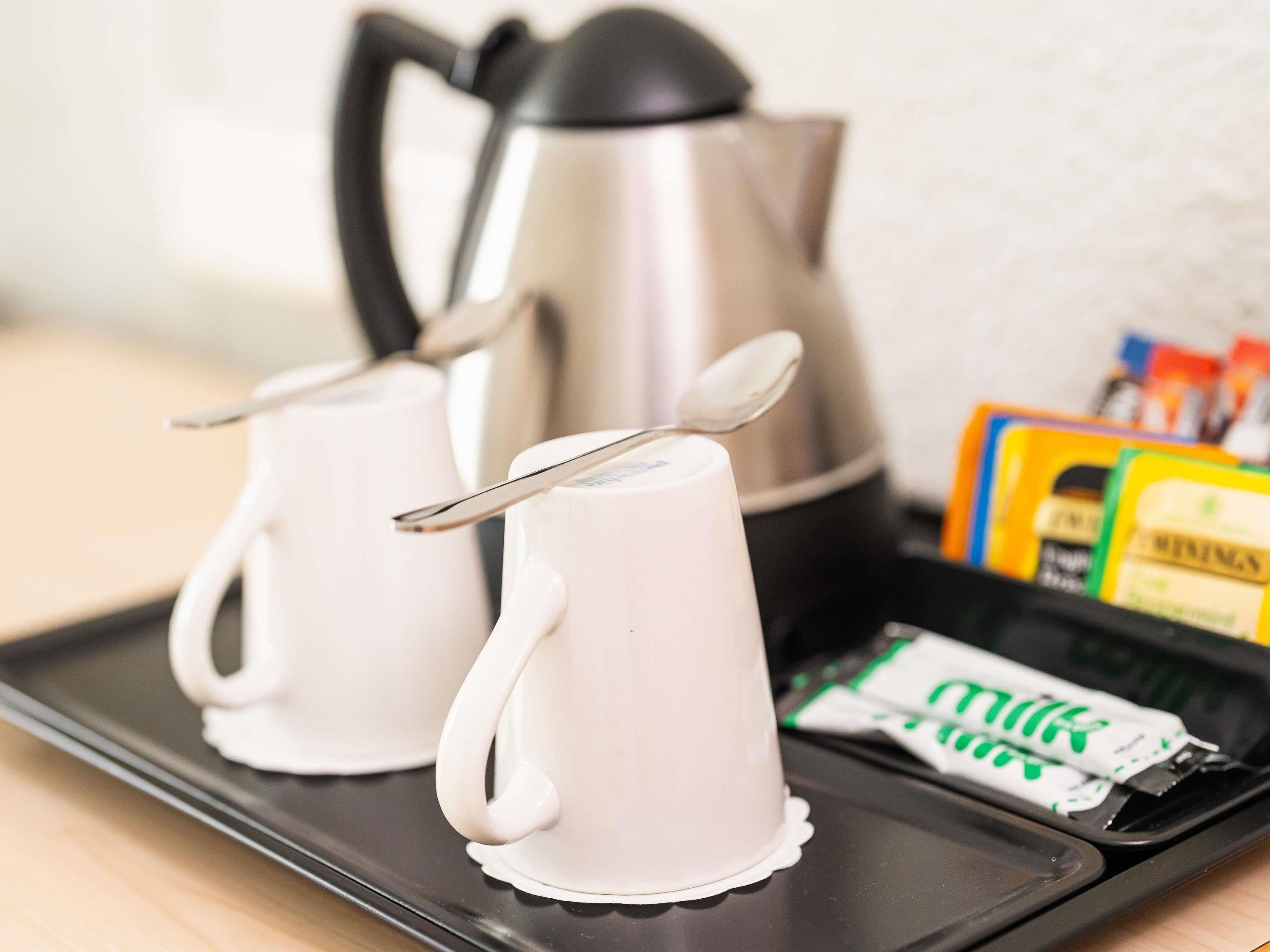 Twee witte bekers met handvatten, een zilveren koffiepot en een dienblad met melkpakken.