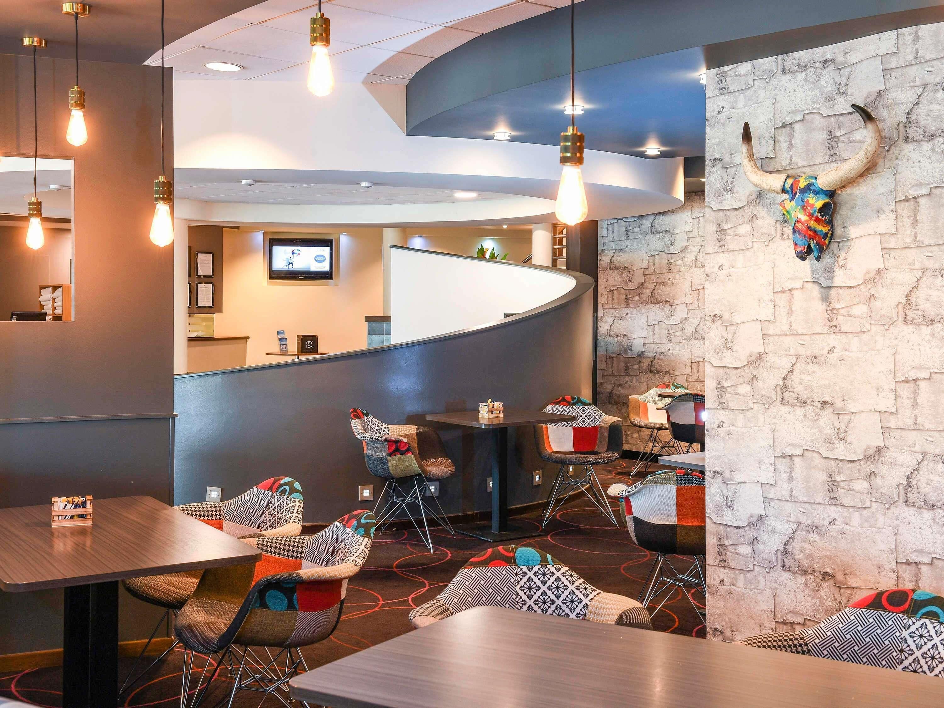 A modern restaurant interior with a curved counter, upholstered chairs, and hanging light fixtures.