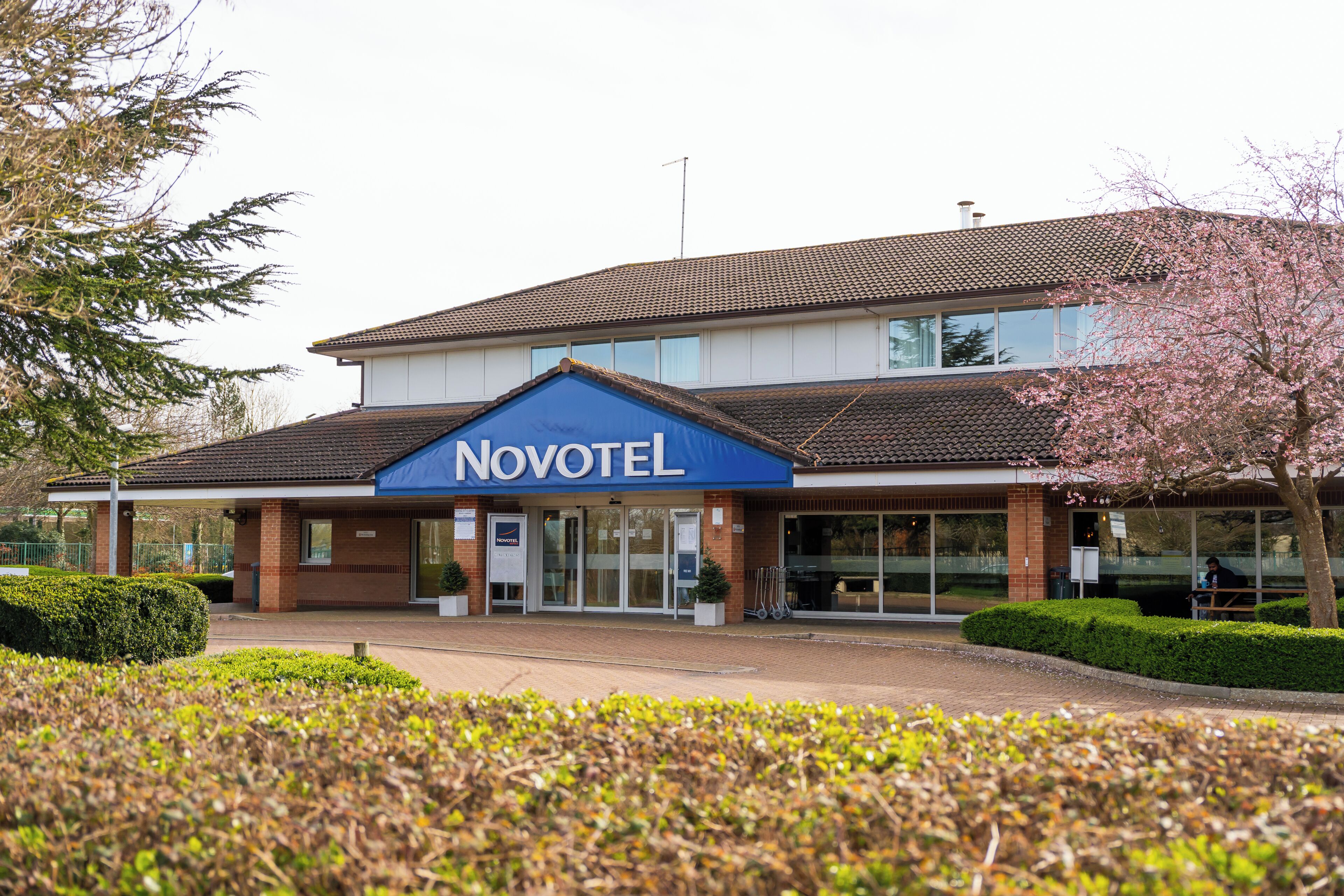 A Novotel hotel with a prominent blue sign, a brick facade, and a parking area in front.